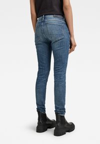 Jeans de denim azul ajustados con una altura media, que cuentan con un diseño clásico de cinco bolsillos y un ligero desgastado. Combinados con botas negras hasta el tobillo.