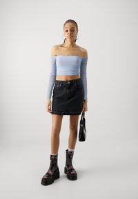 Lyseblå avskåret topp med rynkede lange ermer, parret med en svart denim miniskjørt med frieskant, og kraftige svarte platåstøvler.