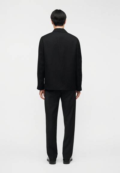 Μαύρο κοστούμι σακάκι και παντελόνι, με λείο ύφασμα, δομημένο σχήμα και απλό σχέδιο χωρίς ορατά μοτίβα ή διακοσμητικά στοιχεία.