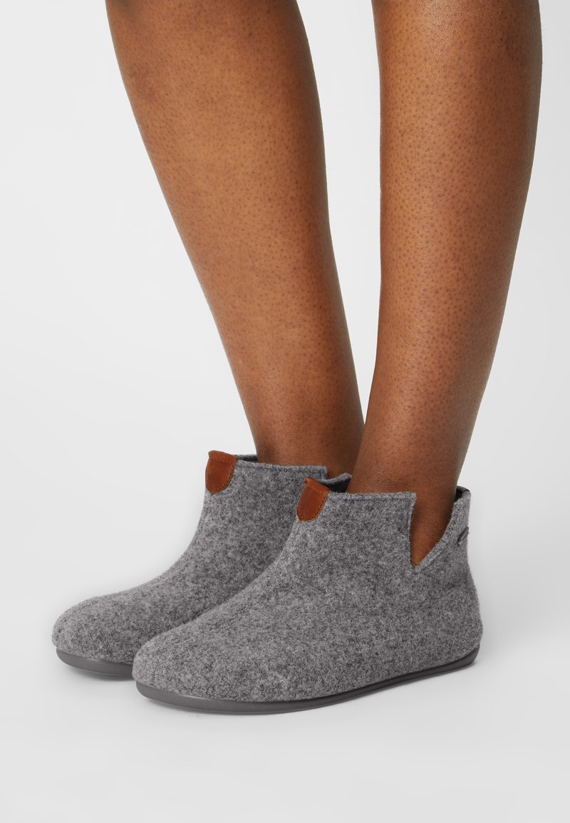 Botines de tobillo grises con acentos de cuero marrón, puntera redondeada y aberturas laterales. Textura suave con una suela de goma flexible para mayor comodidad.