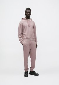 Světlounce růžová mikina s kapucí a odpovídající kalhoty z měkké látky, s nastavovacími šňůrkami, žebrovanými manžetami a bočními kapsami, doplněné černými teniskami.