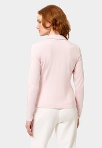Polo a maniche lunghe in morbido tessuto rosa, con colletto classico e una vestibilità su misura, caratterizzato da una texture liscia e orli arrotondati.