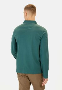 Teal langærmet skjorte med krave, glat tekstur og slim fit, parret med lysebrune bukser. Ingen synlige logoer eller mønstre.