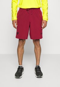 Pantalones cortos deportivos rojos con cintura ajustable, con un logo negro en la pierna izquierda; combinados con una camiseta de manga larga amarilla brillante y zapatos negros.