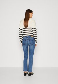Stripete strikkegenser med hette, med marineblå og hvite striper. Brukt sammen med blå rette jeans og svarte flate sko.