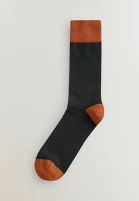 Sort sok med brændt orange kant, hæl og tå, lagt fladt på en lys baggrund.