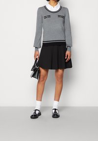 Pull gris clair avec des rayures noires et des zips décoratifs, associé à une jupe noire évasée, des chaussettes blanches et des chaussures noires.