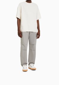 Krämfärgad t-shirt med kort ärm, kombinerad med ljusgrå cargobyxor med flera fickor, bärs med vita sneakers med gummisula.