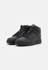 Černé vysoké tenisky s perforovanou špičkou a hladkými koženými panely. Zaoblená špička, pevná gumová podrážka a černé tkaničky.