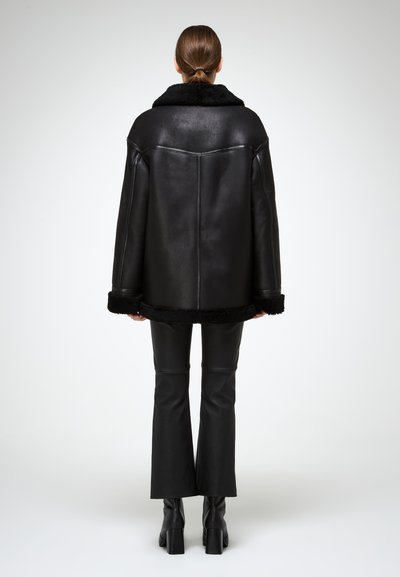 Crna kožna jakna s mekim ovratnikom i manžetama, koja ima opušteni kroj i skrivene šavove. Uparena s crnim trapeznim hlačama i čizmama.