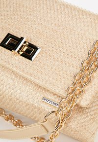 Sac à main tissé beige avec une bandoulière en chaîne dorée, présentant un fermoir rectangulaire noir et doré et une étiquette logo WITTCHEN à l'avant.
