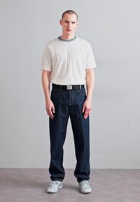 Balta trumpomis rankovėmis marškinėliai su pilku apykakle, derinami su tamsiai mėlynais plačiais džinsais ir baltais sportbačiais; paprastas, laisvalaikio drabužių derinys su minimaliomis detalėmis.