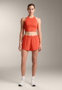 Pomarańczowy sportowy crop top i dopasowane szorty wykonane z gładkiego materiału; top ma wysoki dekolt; szorty mają elastyczny pas i rozcięty dół.