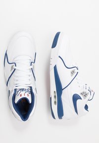 Witte sneakers met marineblauwe accenten, voorzien van een leren bovenwerk, mesh kraag en zichtbare luchtkussens. De veters zijn wit met logo-details op de tong.