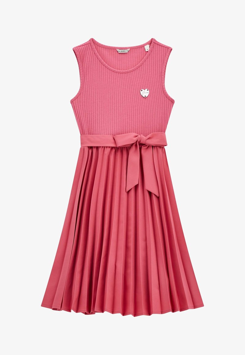 Robe rose sans manches en tissu côtelé avec une jupe plissée, ceinture nouée avec un nœud, et un petit pin's argenté en forme de cœur en accent.