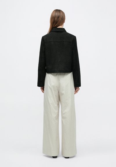 Μαύρο cropped τζάκετ από σουέτ με γιακά, συνδυασμένο με φαρδιά μπεζ παντελόνια. Το ύφασμα φαίνεται απαλό με λεία υφή.