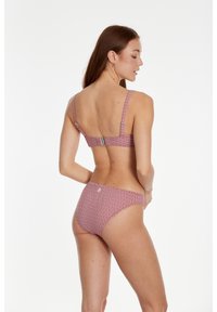 Bikini set s geometrijskim uzorkom u crvenoj i bijeloj boji, sa širokim trakama i kopčanjem straga. Materijal izgleda glatko i rastezljivo.