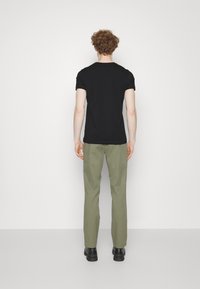 Maglietta nera a maniche corte con scollo rotondo, abbinata a pantaloni verde oliva chiaro e scarpe nere, vista da dietro.