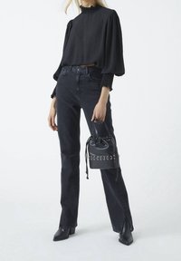 Schwarze strukturierte Bluse mit Puffärmeln und hohem Ausschnitt; kombiniert mit hochgeschnittenen schwarzen Jeans und einer kleinen schwarzen Ledertasche mit Kordelzug.