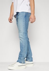 Ljusblå denimjeans med rak passform, med diskret blekning, fem fickor, samt i kombination med vita sneakers.