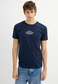 Camiseta de algodón azul marino con texto blanco que dice "NO TOQUES SIN PERMISO." Cuello redondo clásico y mangas cortas.