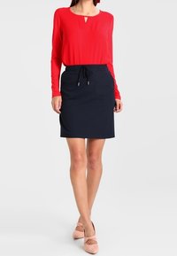 Red long-sleeve top with a keyhole detail; paired with a fitted navy skirt featuring a drawstring waist. Pink ballet flats complete the outfit.