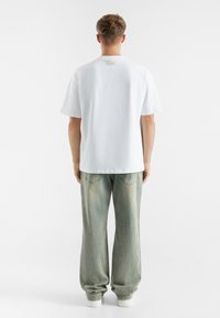 Hvit bomulls t-skjorte med korte ermer, rund hals og logo detalj bak, kombinert med lys blå, vide jeans.
