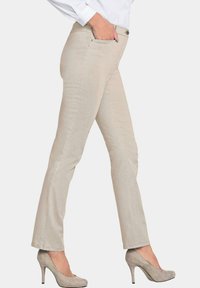Beige slim-fit broek met gestikte zakken, een knoopsluiting en een gladde textuur, gecombineerd met lichtgrijze stilettos.