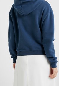 Felpa con cappuccio in cotone blu navy, con polsini e orlo a costine, dalla vestibilità comoda e texture morbida. La vista posteriore mostra il dettaglio del cappuccio.