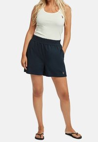 Tummansiniset shortsit, joissa on joustava vyötärönauha ja sivutaskut, yhdistettynä valkoiseen ribbineulottuun toppiin, jossa on pieni kirjailtu yksityiskohta.