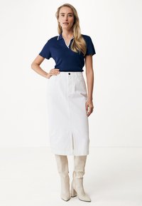 Polo de rayas de color navy con cuello blanco, combinado con una falda midi de denim blanca con una abertura frontal y botas de tobillo beige.