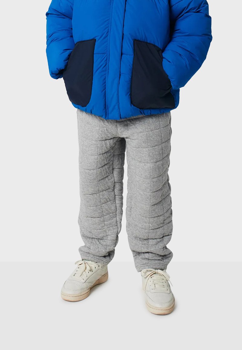 Blaues Daunenjacke mit marineblauen Taschen, kombiniert mit hellgrauen, gesteppten Jogginghosen und weißen Sneakers. Merkmale sind die Daunenstruktur und der Kordelzug.