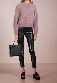 Jasnofioletowy, puszysty sweter z wysokim kołnierzem, czarne skórzane spodnie, czarna torebka z wypukłym napisem „DKNY” oraz czarne sandały na platformie.
