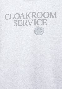 Tricou din bumbac gri cu textul "CLOAKROOM SERVICE" în gri închis, având un design logo circular și anul "1991" sub acesta.