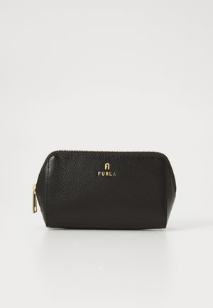 Svart texturerad läderremsväska med guld Furla-logotyp och gulddragkedja, stående upprätt på en vit yta.