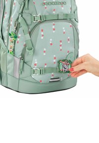 Zaino verde con motivo a pois rosso e bianco, dotato di una toppa di tessuto con un sloth e un tirante della cerniera "Just Chill".