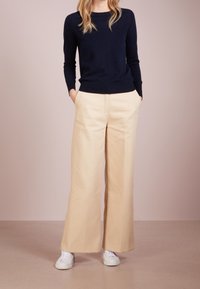 Marinblå stickad tröja med rund halsringning, beige vida byxor, vita sneakers; slät yta och rena, minimala designdetaljer.