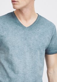 Camiseta azul claro con cuello en V, hecha de un tejido suave y ligeramente texturizado. Presenta mangas cortas y un sutil patrón de color desigual.