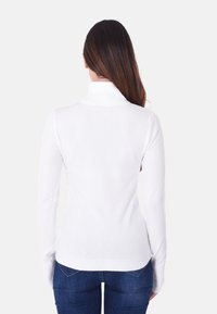 Maglione bianco a collo alto con maniche lunghe, polsini e orlo a costine. Texture liscia, design aderente, indossato con jeans blu scuro.