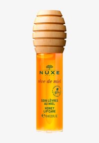 Balsamo labbra al miele di Nuxe in una bottiglietta trasparente da 10 ml con un tappo di legno a forma di favo; liquido arancione vivace; testo verde e viola.
