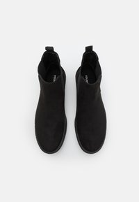 Black suede chelsea ankle boots with elastic side panels and pull tabs. Flat rubber sole, smooth texture, and minimalist design.