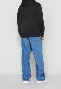 Czarny hoodie z kangurzą kieszenią, zestawiony z luźnymi niebieskimi dżinsami. Całość uzupełniają białe sneakersy.