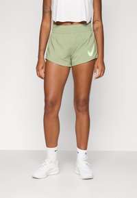 Shorts sportivi verde menta con vita elastica e logo riflettente. Abbinati a scarpe da ginnastica bianche e calzini alti. Design semplice.