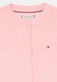 Ανοιχτό ροζ πλεκτό πουλόβερ με ριγέ υφή, διαθέτει τέσσερα κουμπιά, στρογγυλή λαιμόκοψη και ένα μικρό λογότυπο στην αριστερή πλευρά.