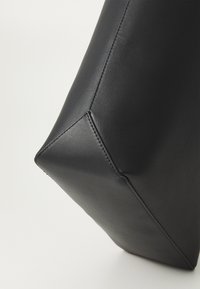Borsa in pelle nera con forma geometrica, dotata di angoli cuciti e texture liscia. Vista angolata che mette in risalto il suo design strutturato.