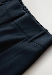 Gros plan sur la ceinture de pantalons bleu marine foncé avec un panneau arrière élastique et une passante de ceinture sur une surface plane.