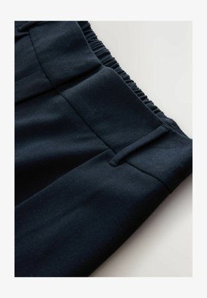 Närbild av midjan på mörkblå byxor med elastisk bakpanel och bältesöglor på en plan yta.