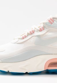 Bílé tenisky s světle modrými semišovými akcenty, růžovými pruhovanými tkaničkami, viditelným vzduchovým polstrováním a modrou gumovou podrážkou na bílém pozadí.