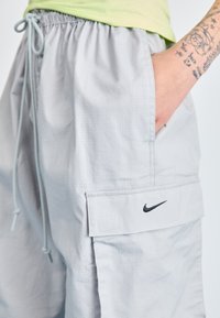 Pantaloni scurți cargo Nike de culoare gri deschis, cu un model texturat în grilaj, talie elastică, buzunar lateral și logo brodat negru pe buzunarul din față.
