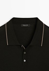 Sort polo skjorte med en kontrasterende beige krave; har tre knapper, ribbet tekstur og et mærke med teksten "Massimo Dutti."